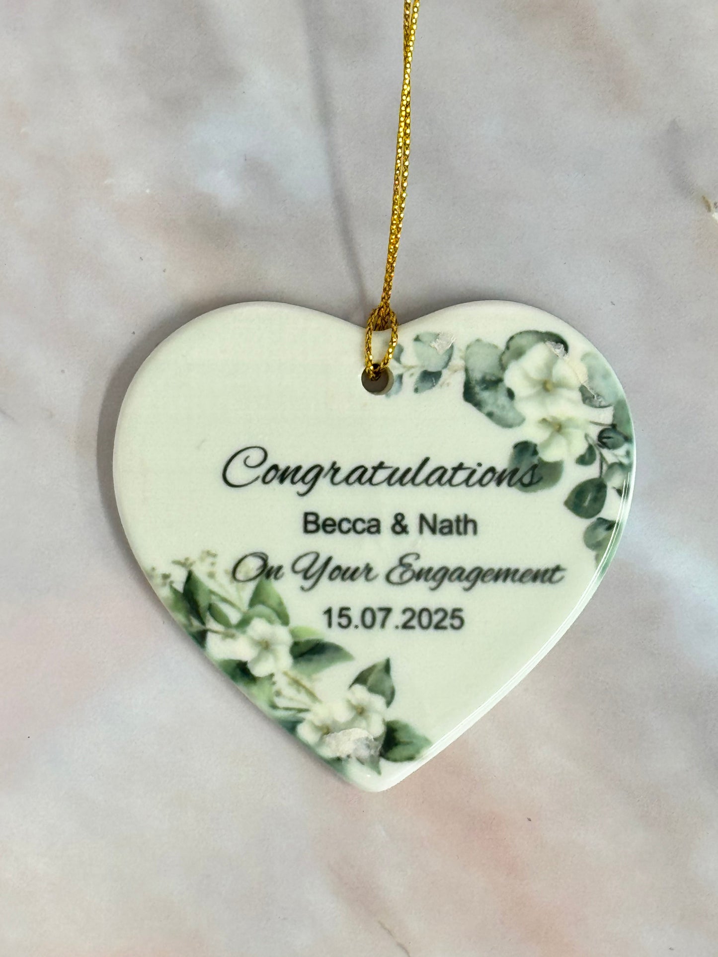 Heart-shaped ceramic ornament with floral designs and engraved text on a marble surface