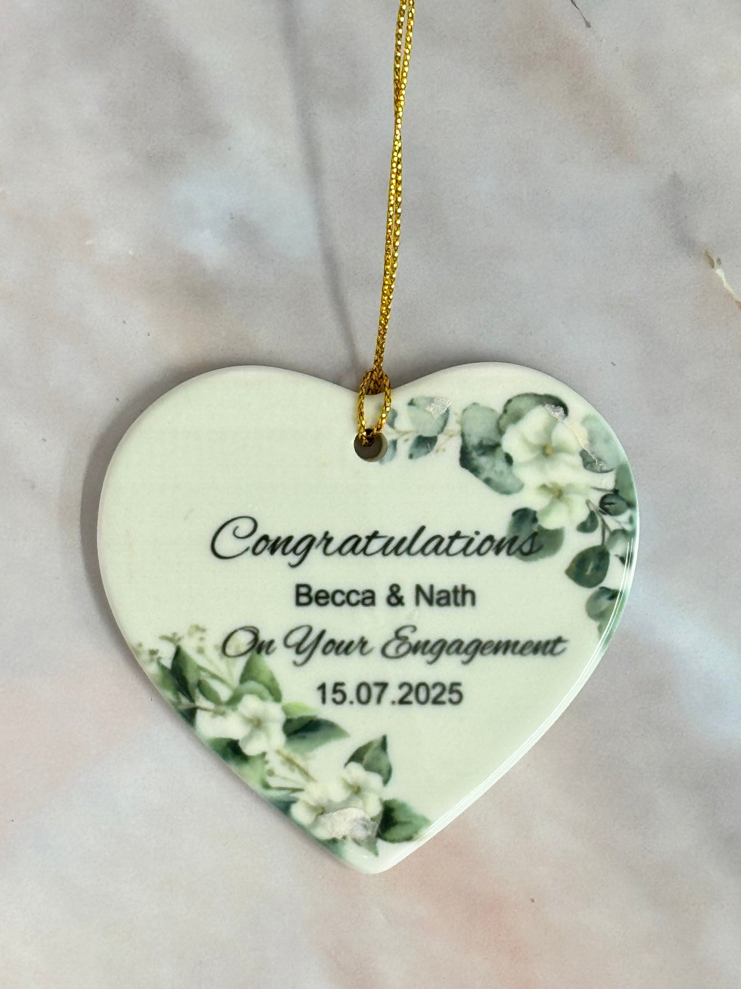 Heart-shaped ceramic ornament with floral design and engraved text on a marble surface